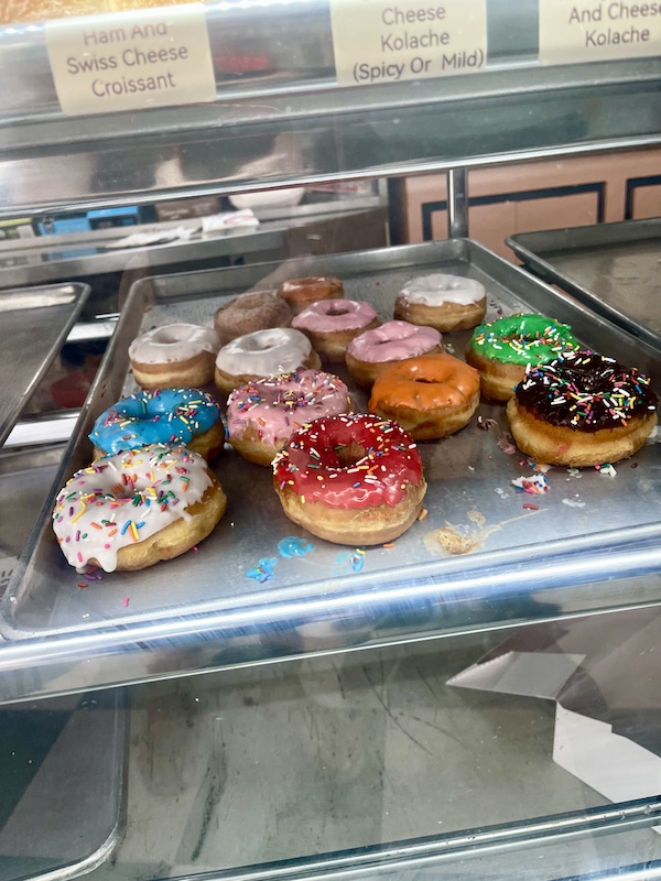 Beside Delicious Texas Kolaches the donut shop sells lots of iced donuts with colorful icing and sprinkles