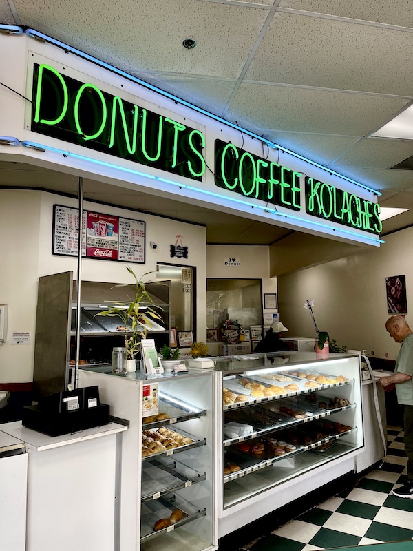 Inside a donut shop with green neon sign over the donut display cases. This is where we tasted out first delicious Texas Kolaches.