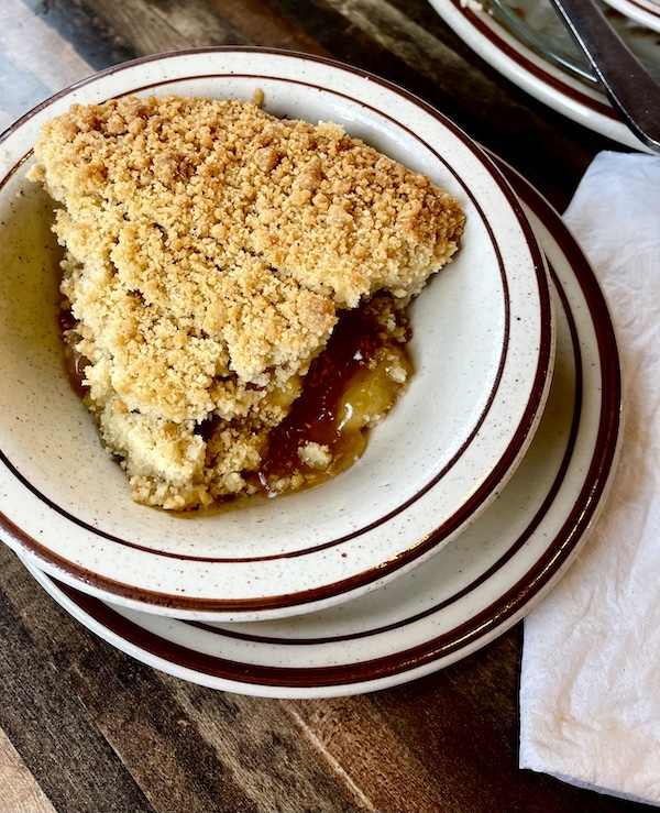 White plate topped with a slice of double crust apple pie with crumb topping at House of Pies Houston Texas