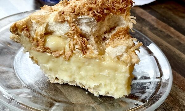 Clear glass plate topped with slice of coconut cream pie with toasted shreds of coconut on top at House of Pies Houston Texas