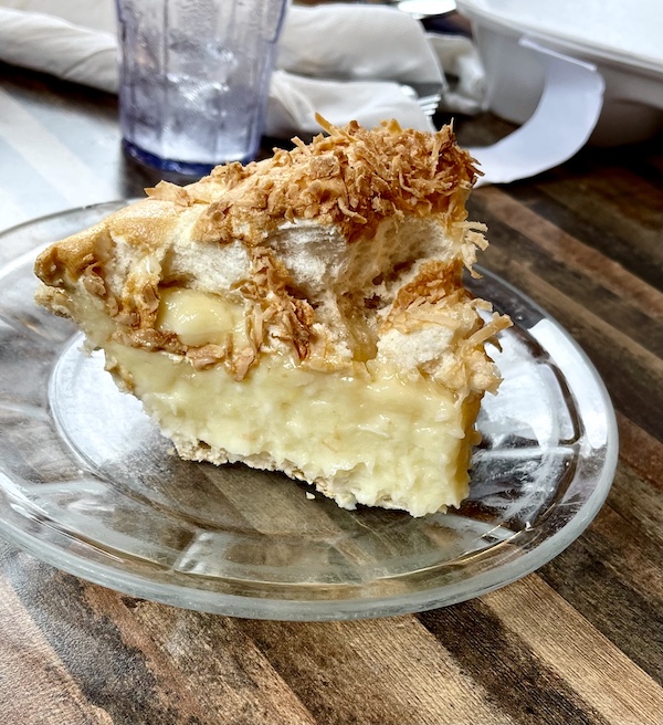 Clear glass plate topped with slice of coconut cream pie with toasted shreds of coconut on top at House of Pies Houston Texas