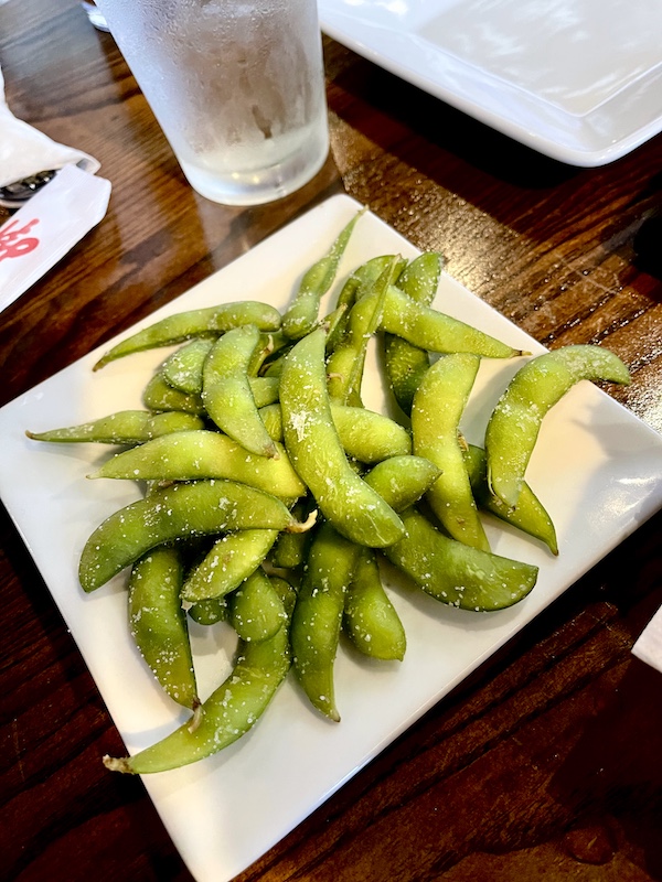 White square plate topped with steamed edamame on the table at Thaicoon Restaurant Pearland Texas
