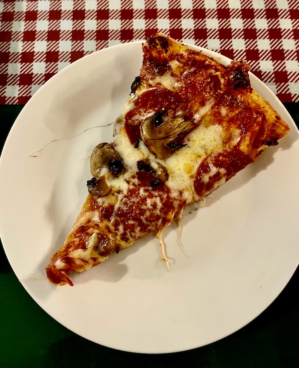 White plate topped with a slice of pizza sitting on a red and white checkered tablecloth at a restaurant in Hill Country's Wimberley Texas