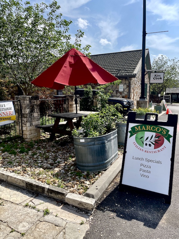 Outside a restaurant with red umbrella and outdoor seating. Sign let's you know it's Marco's in Hill Country's Wimberley Texas