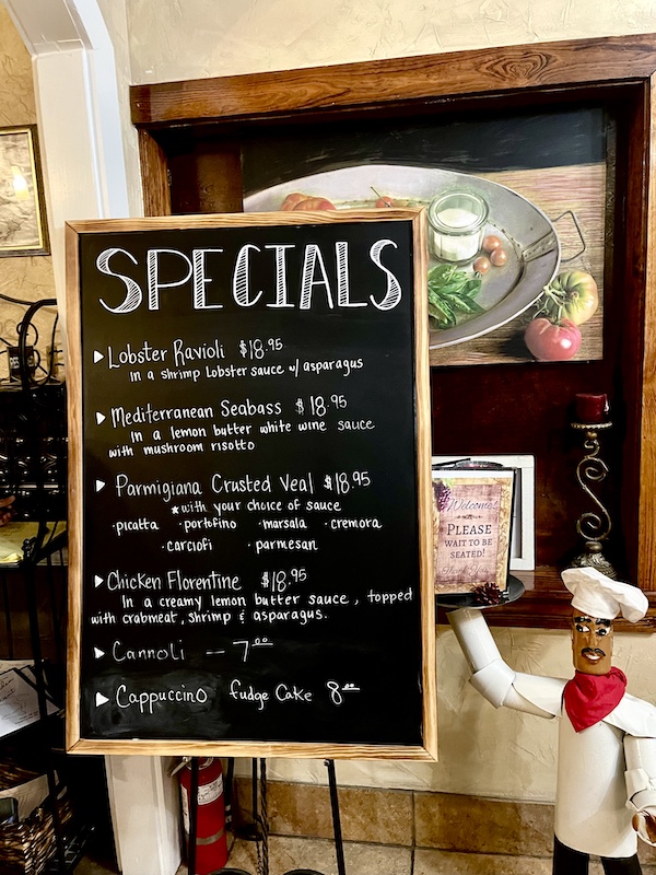 Chalkboard with specials at Italian Garden Restaurant Canyon Lake TX and a little chef sculpture pointing to it.