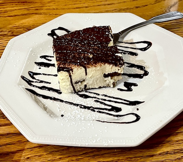 Octagonal white plate topped with a square of tiramisu that's drizzled with chocolate sauce at Italian Garden Restaurant Canyon Lake TX