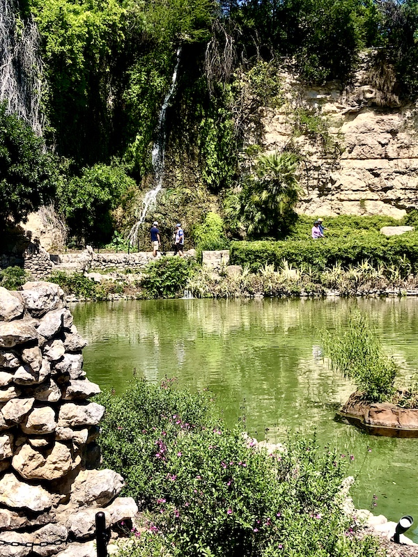 Limestone walls line the green water that reflects the Japanese Tea Garden San Antonio