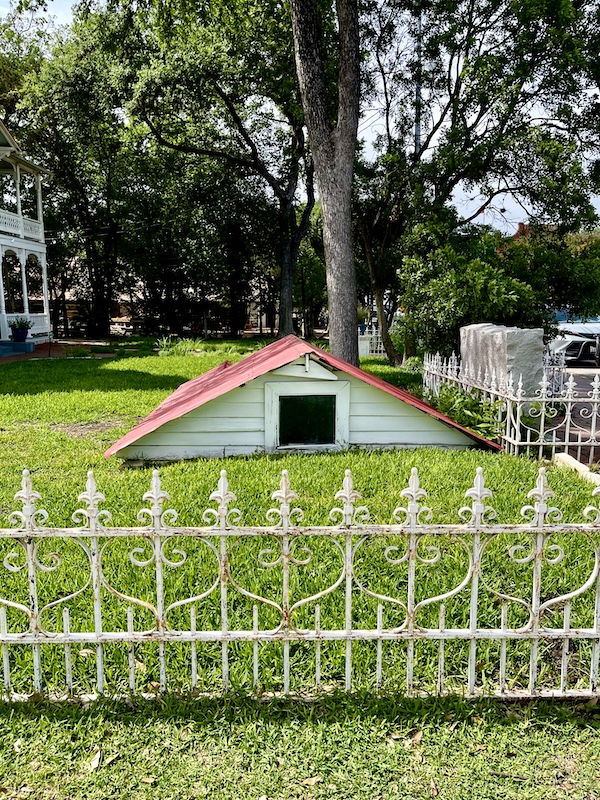 Peaked red roof and white siding of root cellar appears to pop up from the lawn at Gruene Mansion 