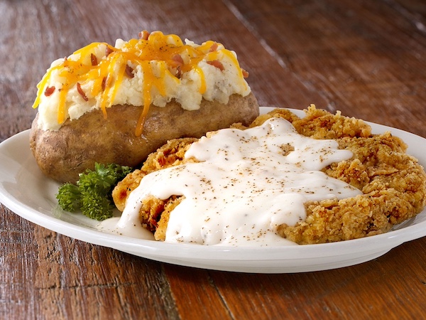White plate topped with chicken fried steak covered in white gravy and loaded baked potato in New Braunfels and Gruene Texas