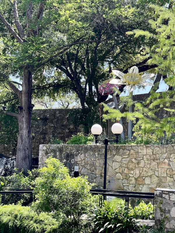 Metal flowers among real trees and plants along San Antonio River Walk