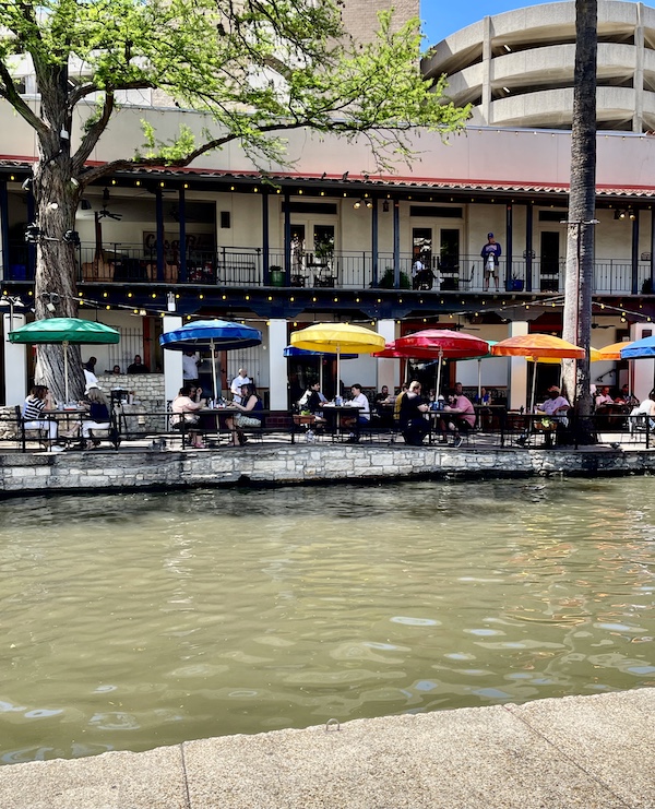 Colorful market umbrellas shade diners at restaurant along San Antonio River Walk