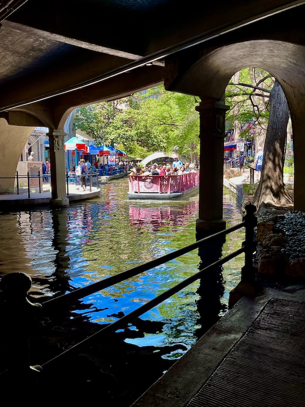 Colorful river boats cruise under the bridge at San Antonio River Walk