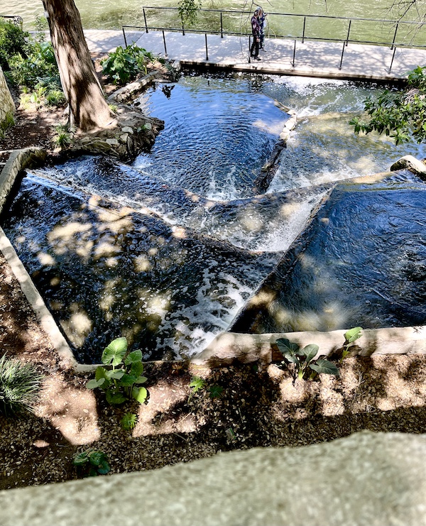 Trees and waterfalls flowing into the river at San Antonio River Walk, seen from above.