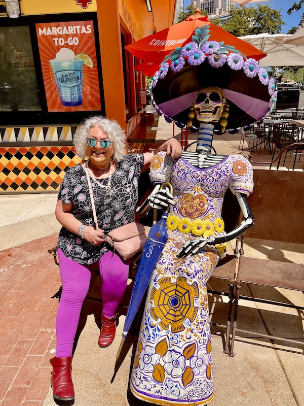 Me sitting on a bench next to a skeleton in a dress with a sombrero after our visit to San Antonio River Walk