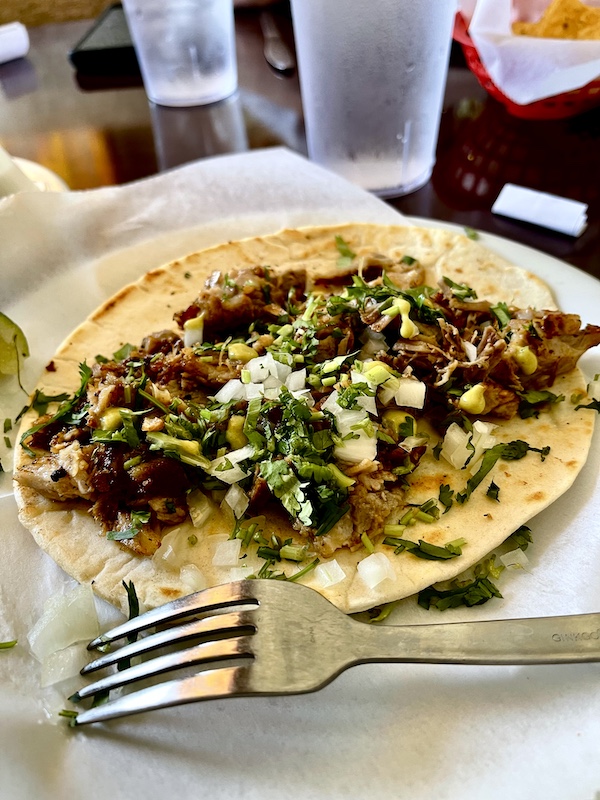 White plate topped with tortilla, shredded pork, onions and salsa for breakfast before our Sunday Funday Fredericksburg Texas