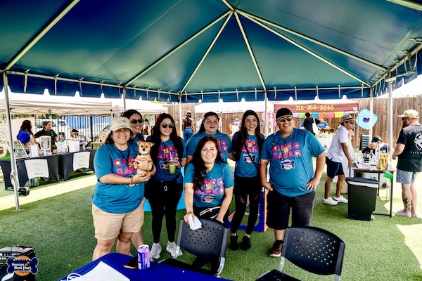 Group of people in teal t-shirts under a tent at Cinco de Barko Houston