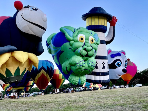 Ladybug, cat, lighthouse and raccoon hot air balloons tethered at the Hopkins County Dairy Festival 2025