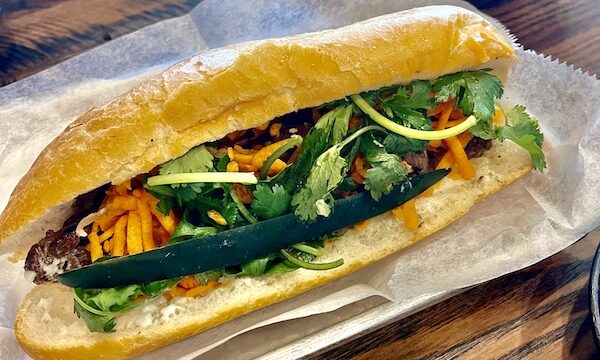 Rectangular white plate topped with a hero roll filled with sliced pork, carrots, radish and cucumber was a Taste Vietnam in Houston TX