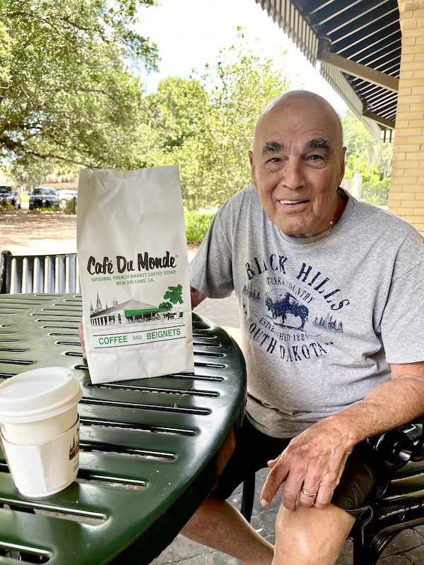 Steve sitting outside at a table with a bag from Cafe du Monde during our Bonus Visit to NOLA