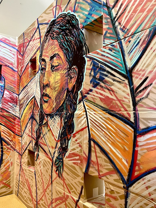 Mural of the head of a Native American woman with black hair and pigtails peaking out among colorful leaves painted on cardboard at Westmoreland Museum of American Art 2