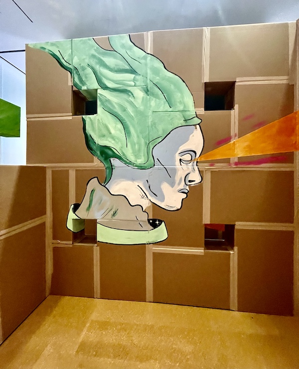 Mural of a woman with green hair and orange beam coming from her eyes painted on cardboard at Westmoreland Museum of American Art 2