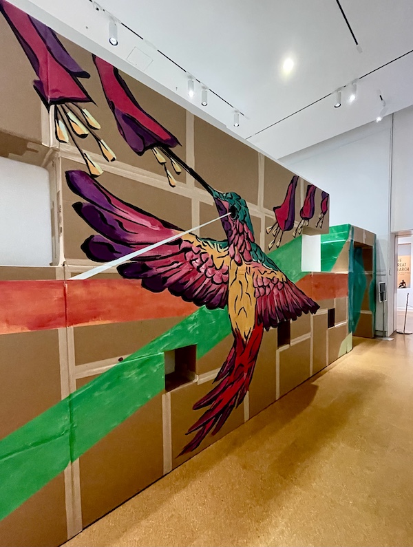 Mural of a hummingbird with beak in a dark red flower painted on cardboard at Westmoreland Museum of American Art 2