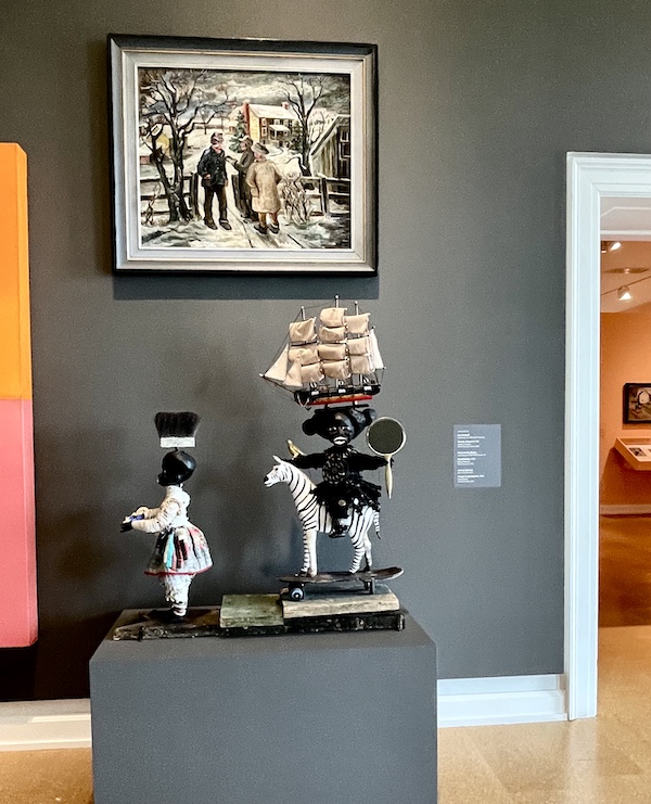 Gray wall with a painting hung above mixed media figures of primitive design at the Westmoreland Museum of American Art