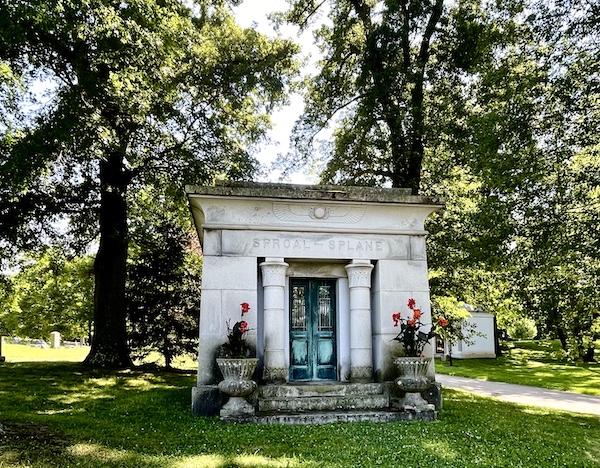Small white classic greek mausoleum with metals doors that have turned shades of green at Allegheny Cemetery Pittsburgh Pennsylvania