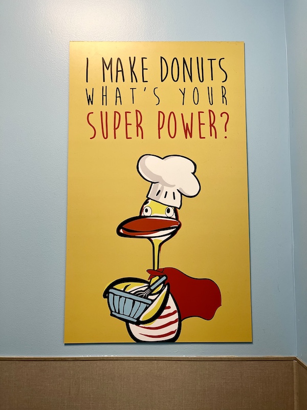 Bright yellow sign on a wall showing a duck with a chef hat holding a donut.