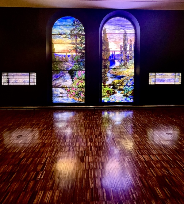 Pair of arched colorful stained glass windows at reflecting onto a wood floor at Allentown Art Museum