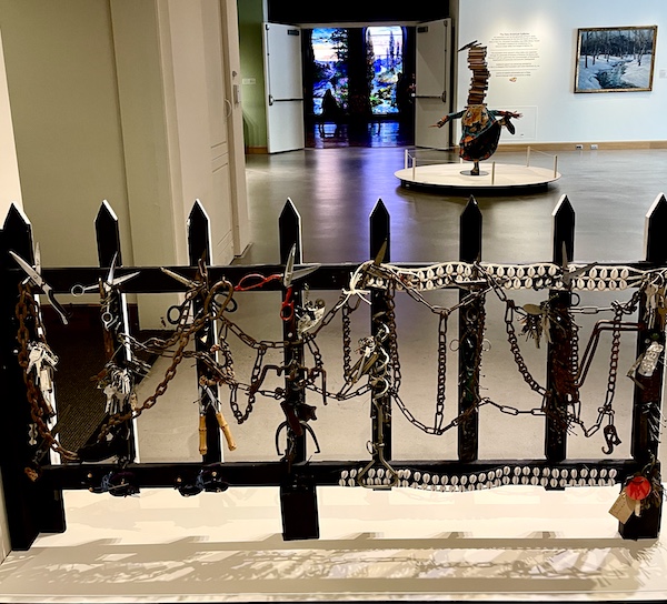 Picket fence that's white on one side and black on other. Black side showing with all sorts of found objects attached to fence at Allentown Art Museum