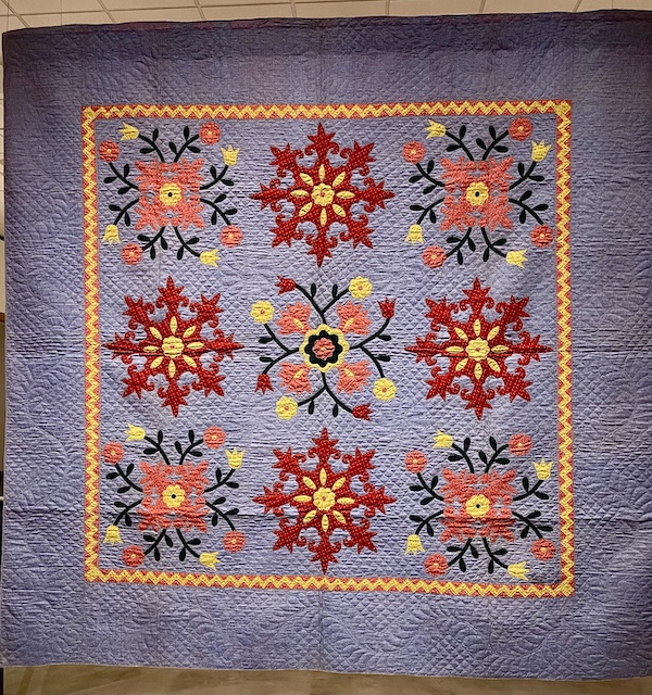 Lavender quilt with a variety of red flowers in center at Allentown Art Museum Quilts