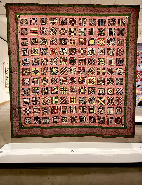 Quilt with coral colored background and small squares of different patterns at Allentown Art Museum Quilts
