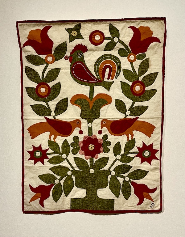 Small rectangular quilt with ivory background and multicolored rooster, birds and florals at Allentown Art Museum Quilts