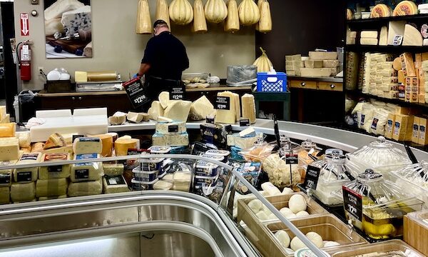 DeLallo Italian Marketplace refrigerator case of more cheeses including 2 different varieties hanging from the ceiling.