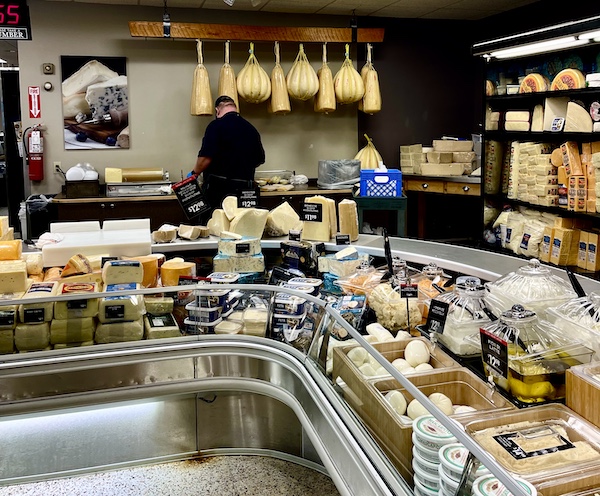 DeLallo Italian Marketplace refrigerator case of more cheeses including 2 different varieties hanging from the ceiling.