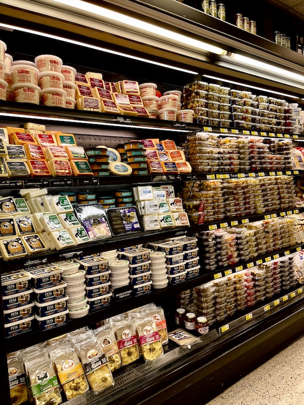 DeLallo Italian Marketplace refrigerator wall case of packages of prepared foods, ravioli, cheese and olive bar items
