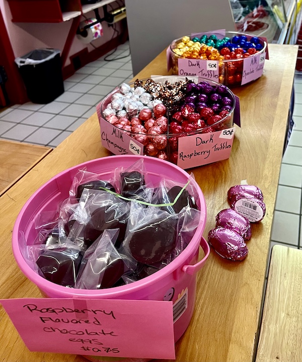 Pink sand bucket filled with dark chocolate and glass bowls filled with foil wrapped chocolate truffles on a wood shelf at Wilson Candies Jeannette PA