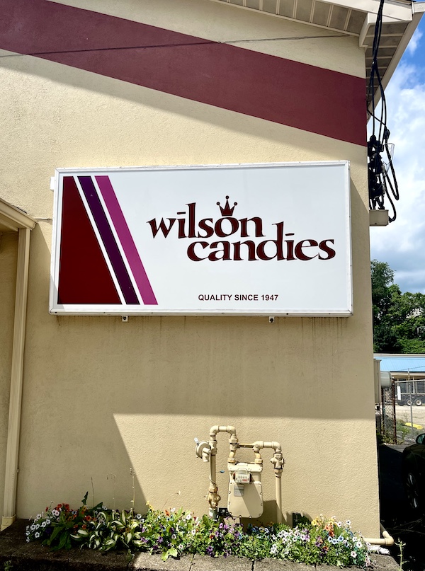 White and burgundy sign for Wilson Candies Jeannette PA on pale yellow building