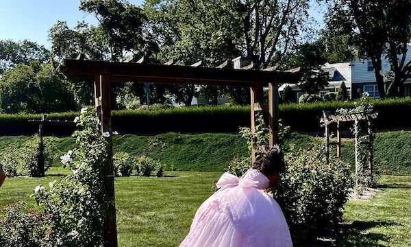 Girl in light pink gown pretending to hide behind a wood arbor at the Malcolm Gross Rose Garden