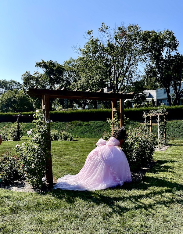 Girl in light pink gown pretending to hide behind a wood arbor at the Malcolm Gross Rose Garden