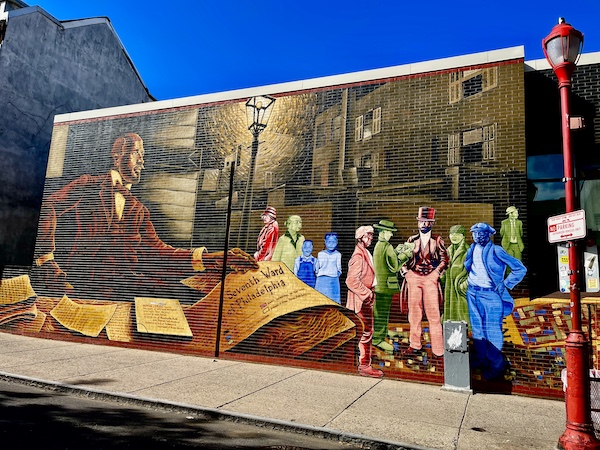 Painting on brown brick building depicting people throughout Philadelphia history is another example of the Murals Around Philadelphia