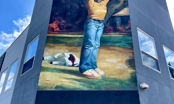 Mural of a boy in jeans with arms up on corner of building is one of the Murals Around Philadelphia