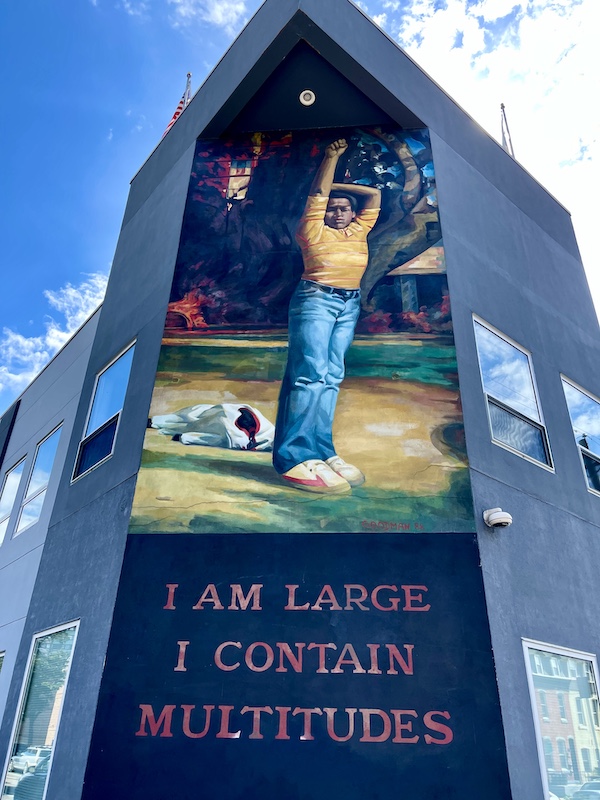Mural of a boy in jeans with arms up on corner of building is one of the Murals Around Philadelphia