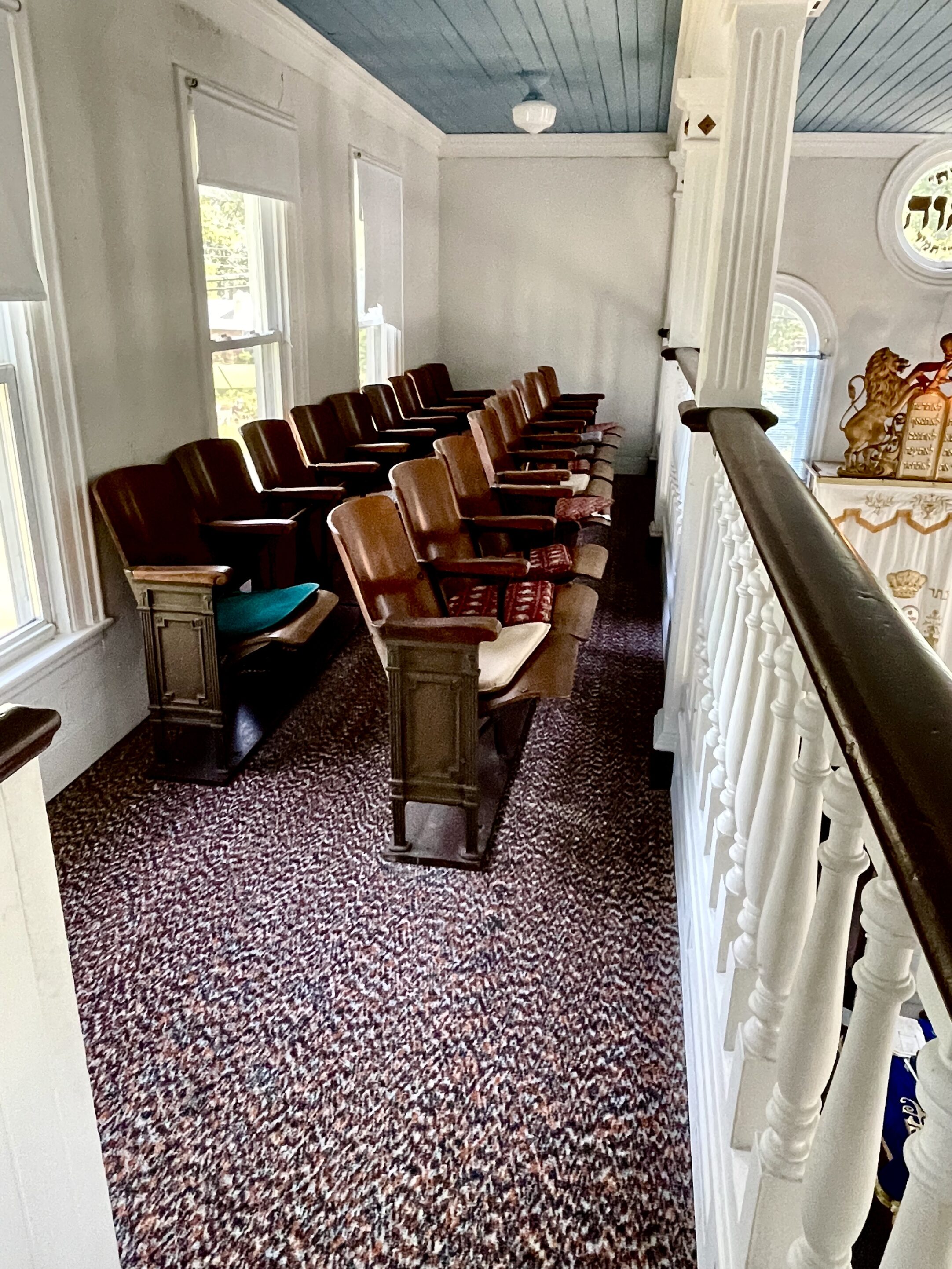 Two rows of dark brown wood chairs against a white rail for women at the Alliance Synagogue and Cemetery Pittsgrove NJ