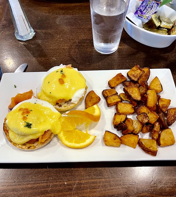 White rectangular plate topped with 2 English muffin halves with smoked salmon and hollandaise sauce accompanied by home fries at Johnny's Café Margate NJ