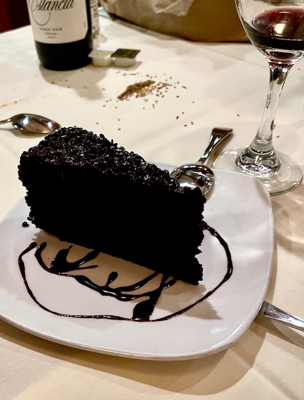 White plate topped with a large slice of very dark chocolate cake with a circle of chocolate sauce on plate about slice at Sapore Woodfire Pizza and Restaurant