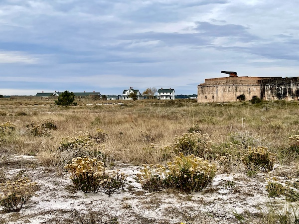 Cannon atop a brick fort wall, grasses and sand, with white houses in background at Fort Pickens Pensacola Florida