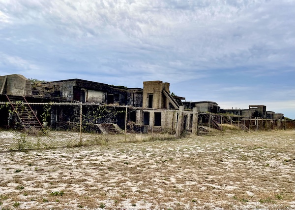 Buildings that were once barracks at Fort Pickens Pensacola Florida are in ruins and behind chain link fence.