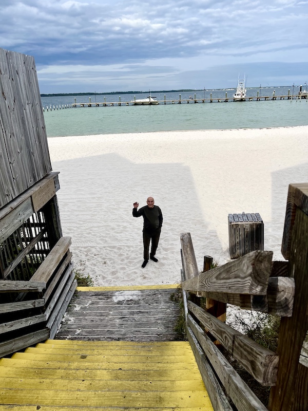 Pensacola Beach and Boardwalk where Steve is waving from the bottom of the steps on the white sand beach with Gulf in background
